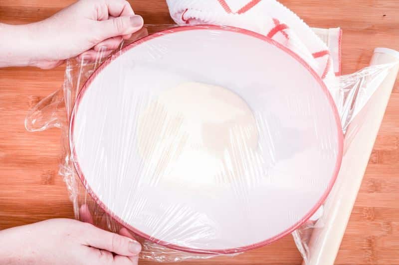 How to Make Pretzel Bread Step 10-2 Covering dough in bowl with plastic wrap.