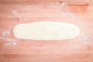 Dough formed into a long roll on floured surface.
