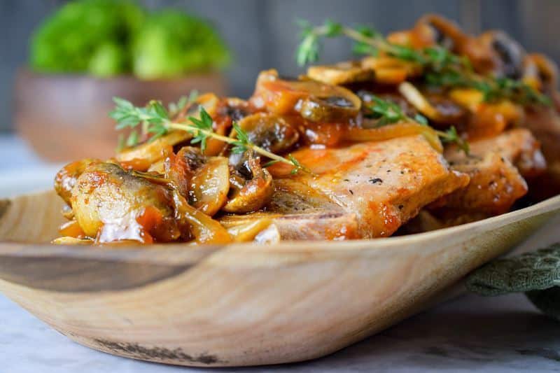 Electric Skillet Pork Chops on a wooden serving platter with a bowl of broccoli on the side.
