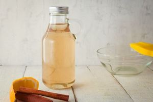 A glass bottle of simple syrup, cinnamon and orange on the side.