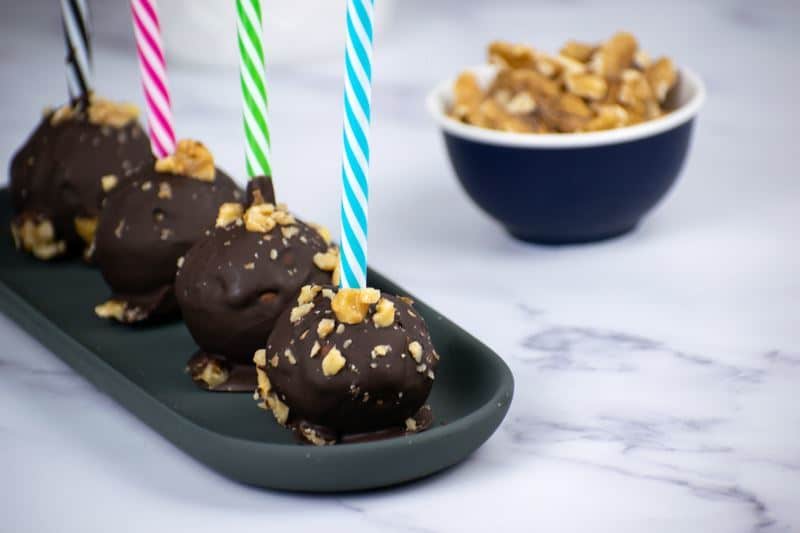 Banana cake pops upside down on a black tray with colorful, striped treat sticks.