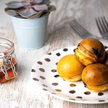 Pancake cake pops on a white plate with polka dots, a jar of maple syrup in the background.