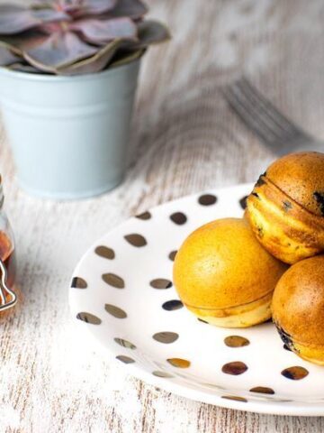 Pancake cake pops on a white plate with polka dots, a jar of maple syrup in the background.