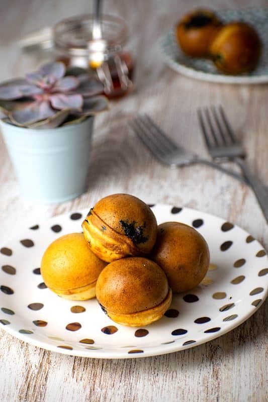 Pancake cake pops on a white plate with polka dots, a jar of maple syrup in the background.