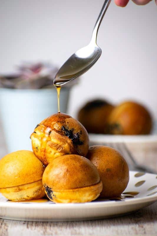 Pancake cake pops covered in maple syrup on a white plate with polka dots.