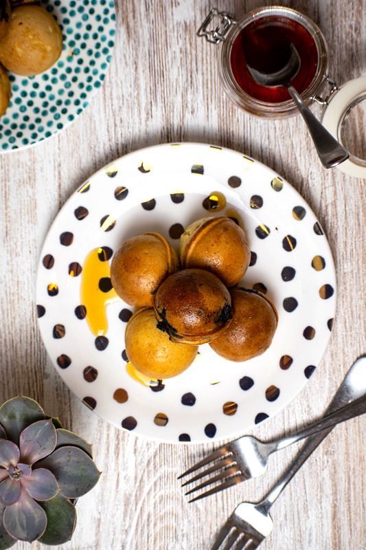 Pancake Cake Pops_6 Pancake cake popPancake cake pops covered in maple syrup on a white plate with polka dots.s on a white plate with polka dots, a jar of maple syrup in the background.
