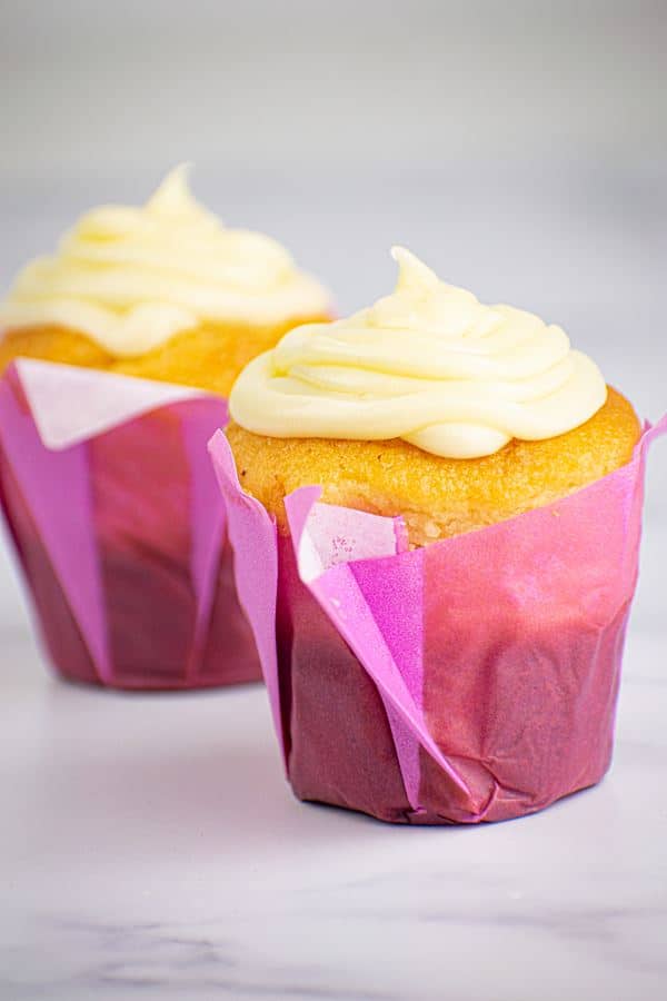 Butter Cream_2 2 cupcakes with buttercream frosting in purple wrappers.