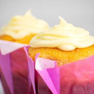 2 cupcakes with buttercream frosting in purple wrappers.