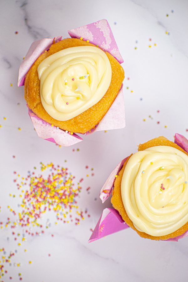 Butter Cream_6 2 cupcakes with buttercream frosting in purple wrappers, sprinkles on the side.
