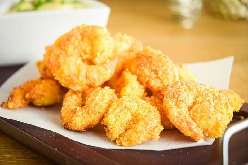 Fried coconut shrimp on a black serving tray, curry dip on the side.