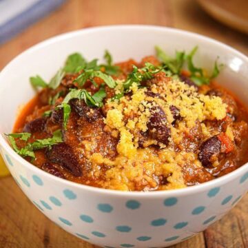 Electric Skillet Chili in a white bowl with blue polka dots, wooden background, tortillas chips on the side.