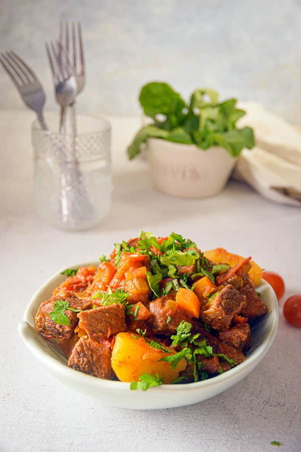 Classic Beef Stew with Potatoes and Carrots_2 Electric Skillet Beef Stew in a white bowl, cherry tomatoes and forks on the side, white background.