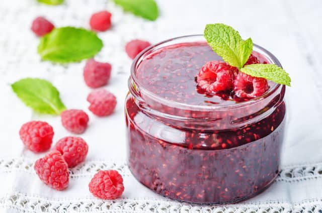 raspberry jam on a white background. the toning. selective focus Raspberry jam on a white background, with raspberries on the side.