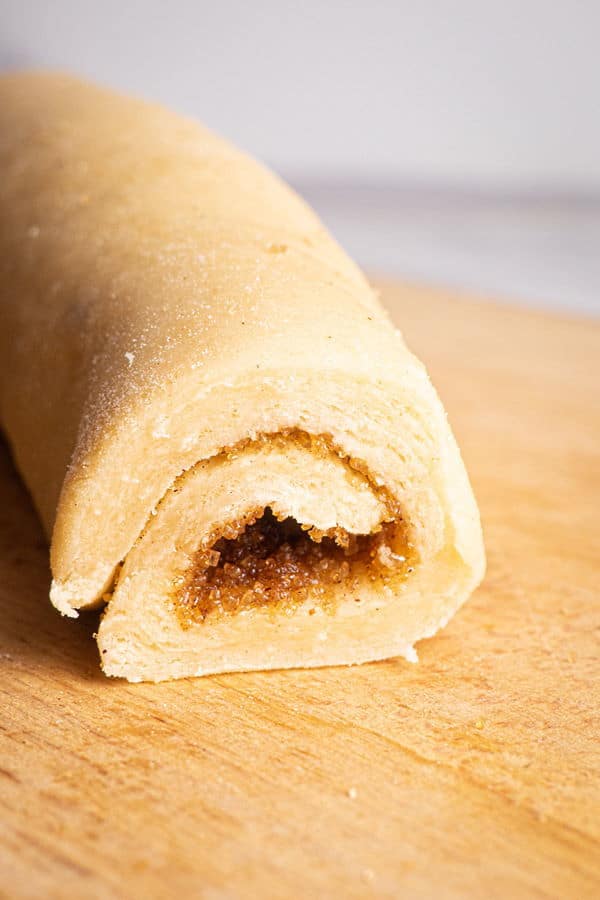 How to Make Cinnamon Rolls_16 Raw cinnamon bun roll on wooden cutting board.
