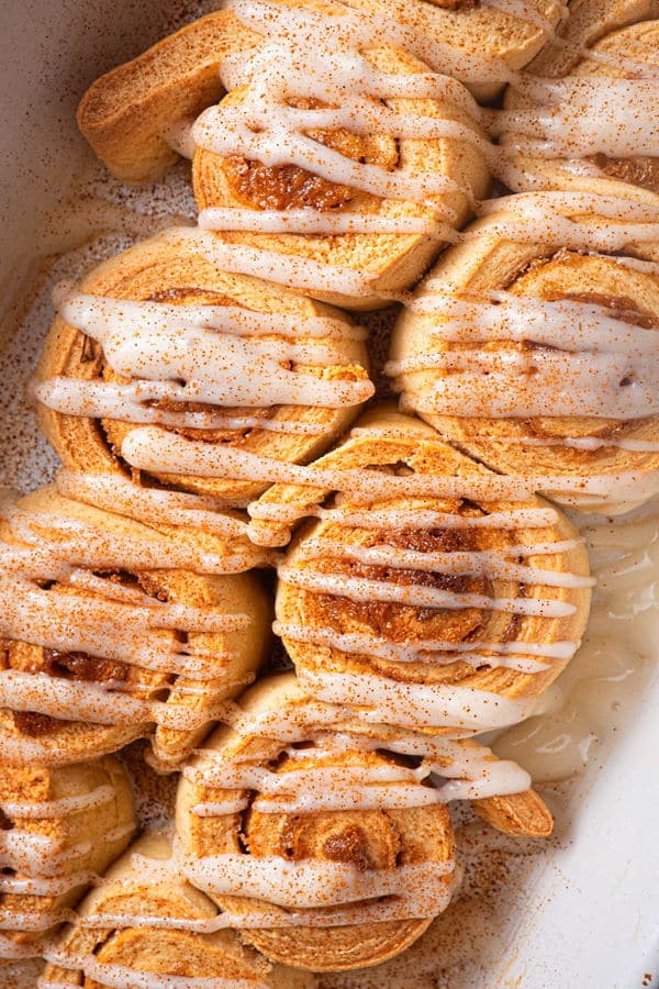 How to Make Cinnamon Rolls_20 Cinnamon Buns with cream cheese frosting drizzled on top in white serving dish.