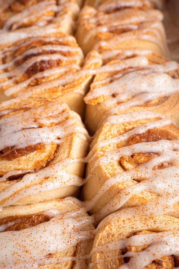 How to Make Cinnamon Rolls_22 Cinnamon Buns with cream cheese frosting drizzled on top in white serving dish.