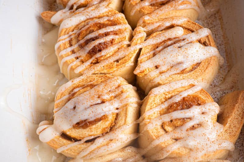 How to Make Cinnamon Rolls_23 Cinnamon Buns with cream cheese frosting drizzled on top in white serving dish.
