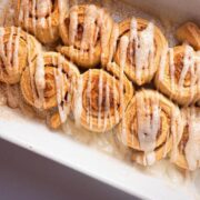 Cinnamon Buns with cream cheese frosting drizzled on top in white serving dish.
