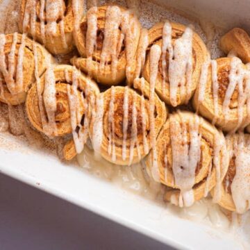 Cinnamon Buns with cream cheese frosting drizzled on top in white serving dish.
