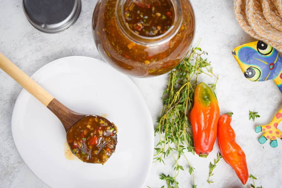 Jerk sauce in a jar with chili peppers, thyme and garlic on the side.