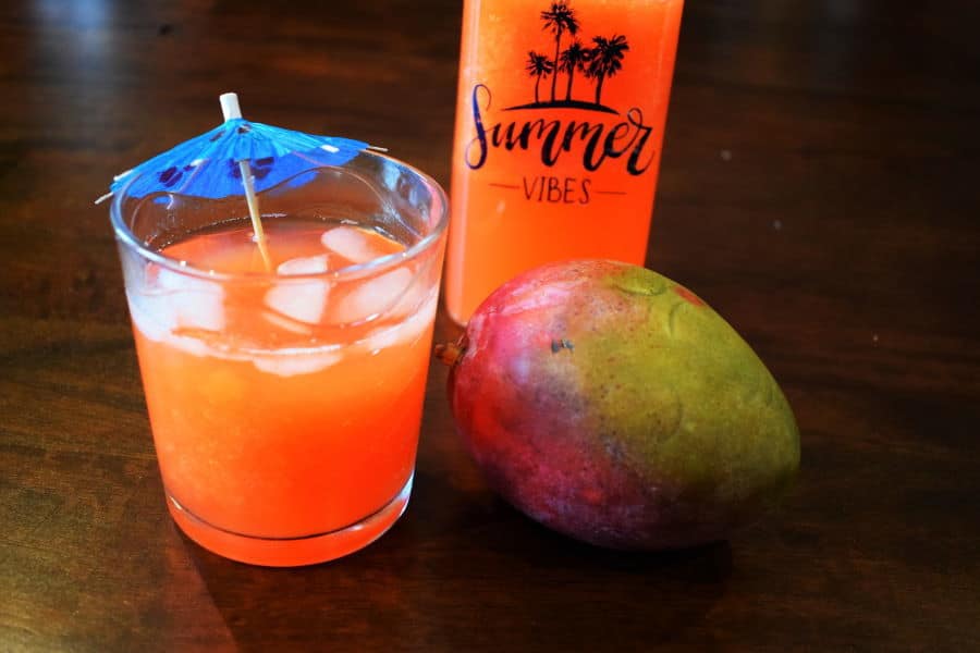 Summer mango soda in a glass with a mango on the side, wood background.