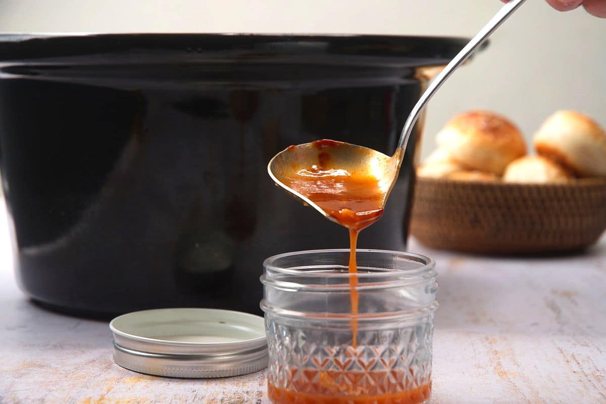 Pulled pork shoulder sauce pouring from spoon into jar.