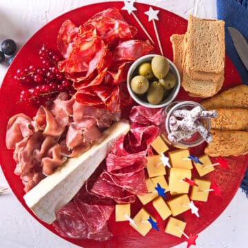 4th of July themed charcuterie board on red plate with red, white and blue stars.