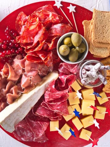 4th of July themed charcuterie board on red plate with red, white and blue stars.