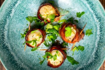 Bacon wrapped scallops with butter sauce in blue dish.