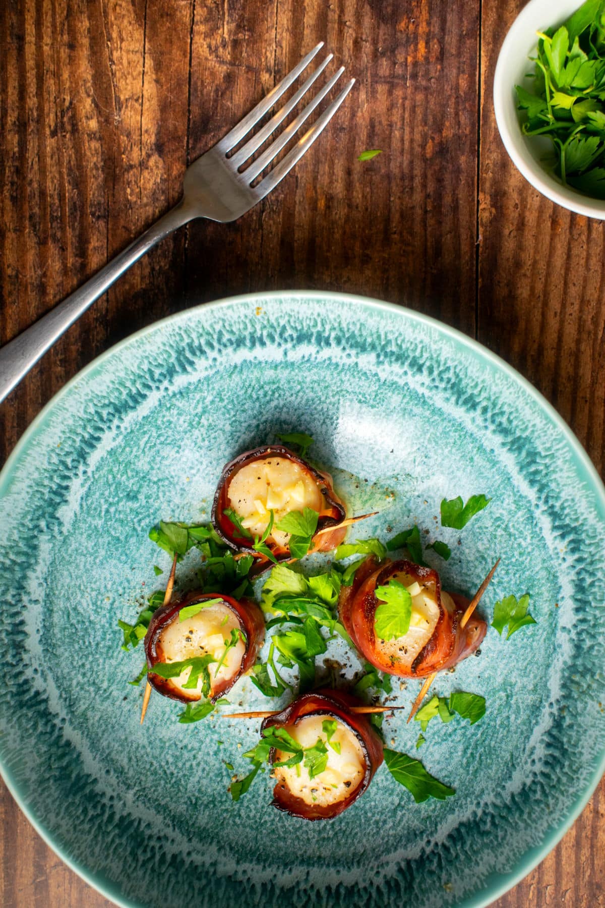 Bacon wrapped scallops with butter sauce in blue dish.