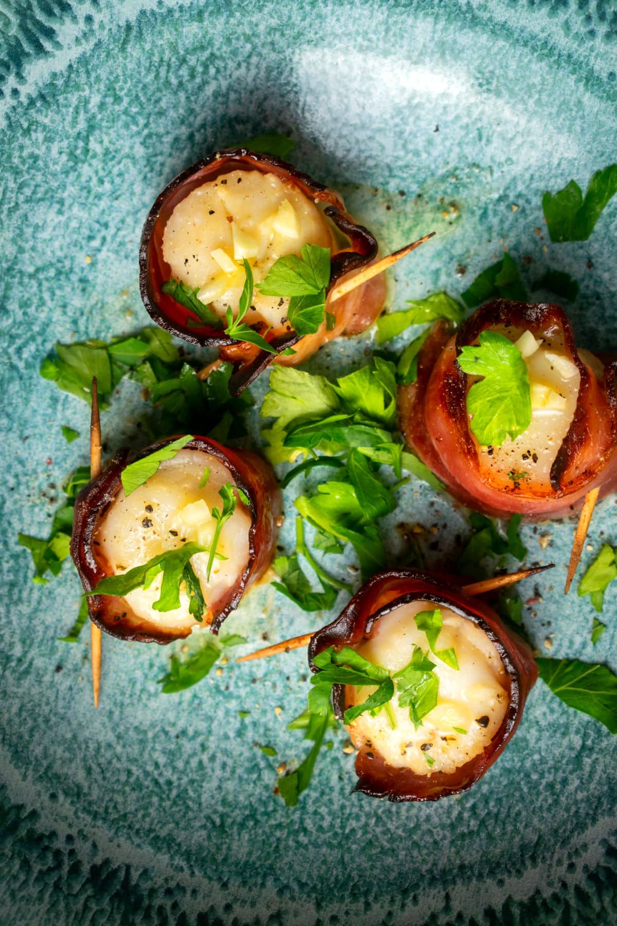 Bacon wrapped scallops with butter sauce in blue dish.