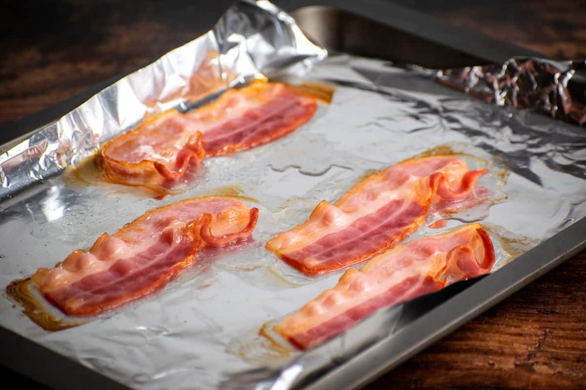 Par-cooked bacon strips on foil lined baking sheet.
