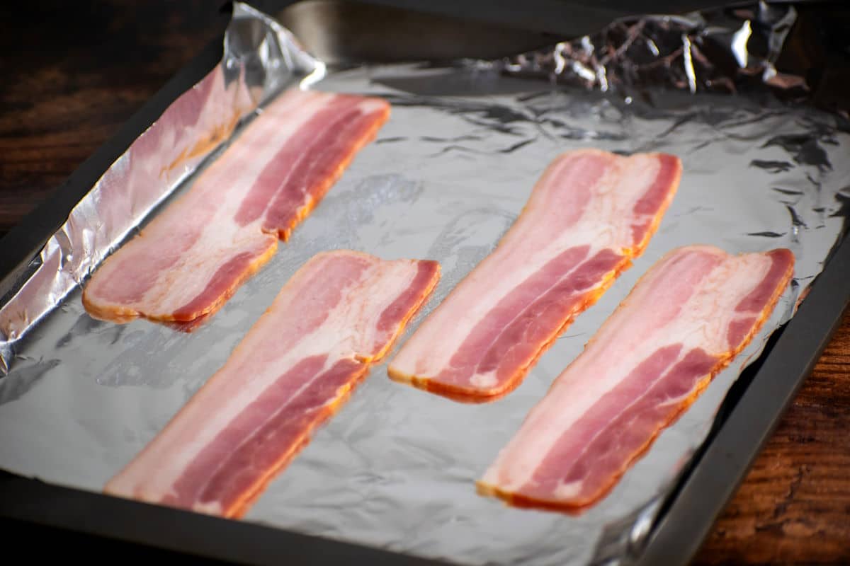 Raw bacon strips on foil lined baking sheet.