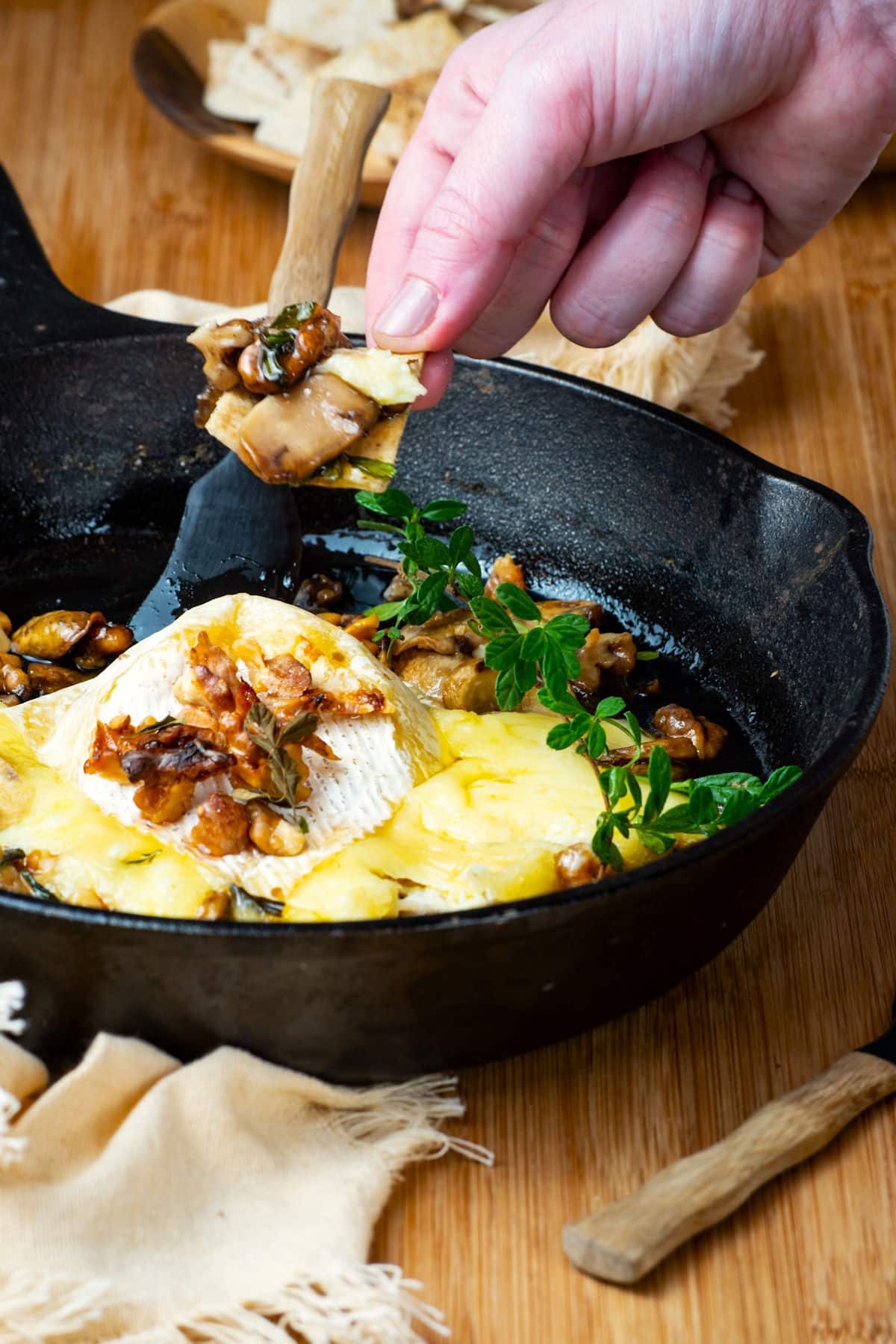 Baked brie in cast iron pan with a hand holding a cracker.