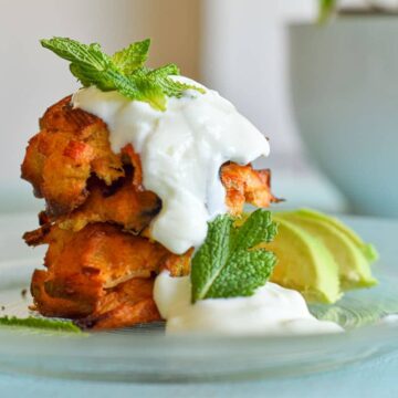 Crab cakes stacked on plate with yogurt, mint and sliced avocado.