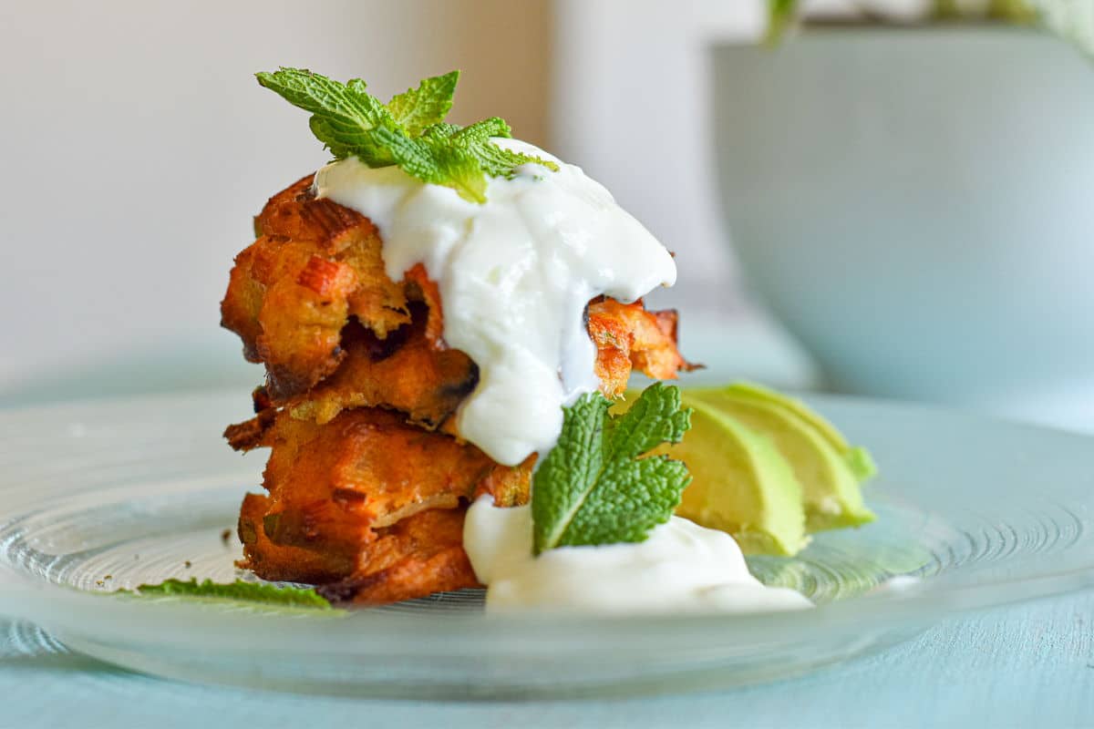 Crab cakes stacked on plate with yogurt, mint and sliced avocado.