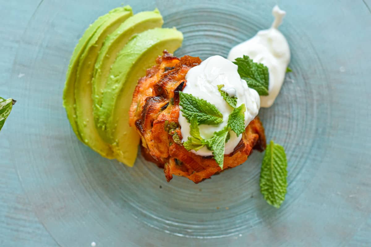 Crab cakes stacked on plate with yogurt and sliced avocado.