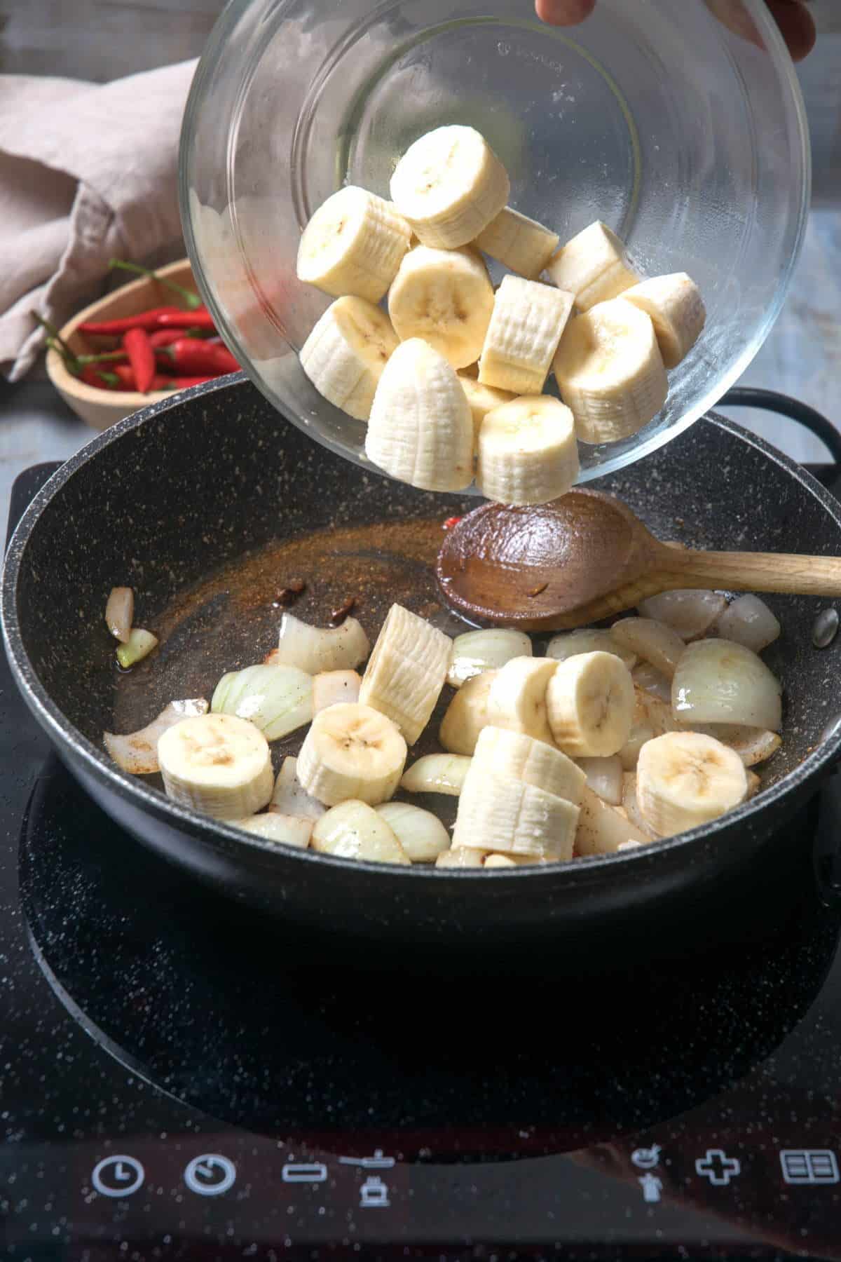 Sliced bananas in a frying pan with onions.