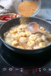 Sliced bananas in a frying pan with apple cider vinegar and brown sugar in a small bowl.