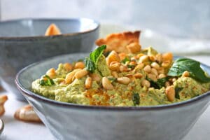 Basil hummus with pine nuts in blue bowl.
