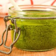Basil pesto in a small jar on wooden table.