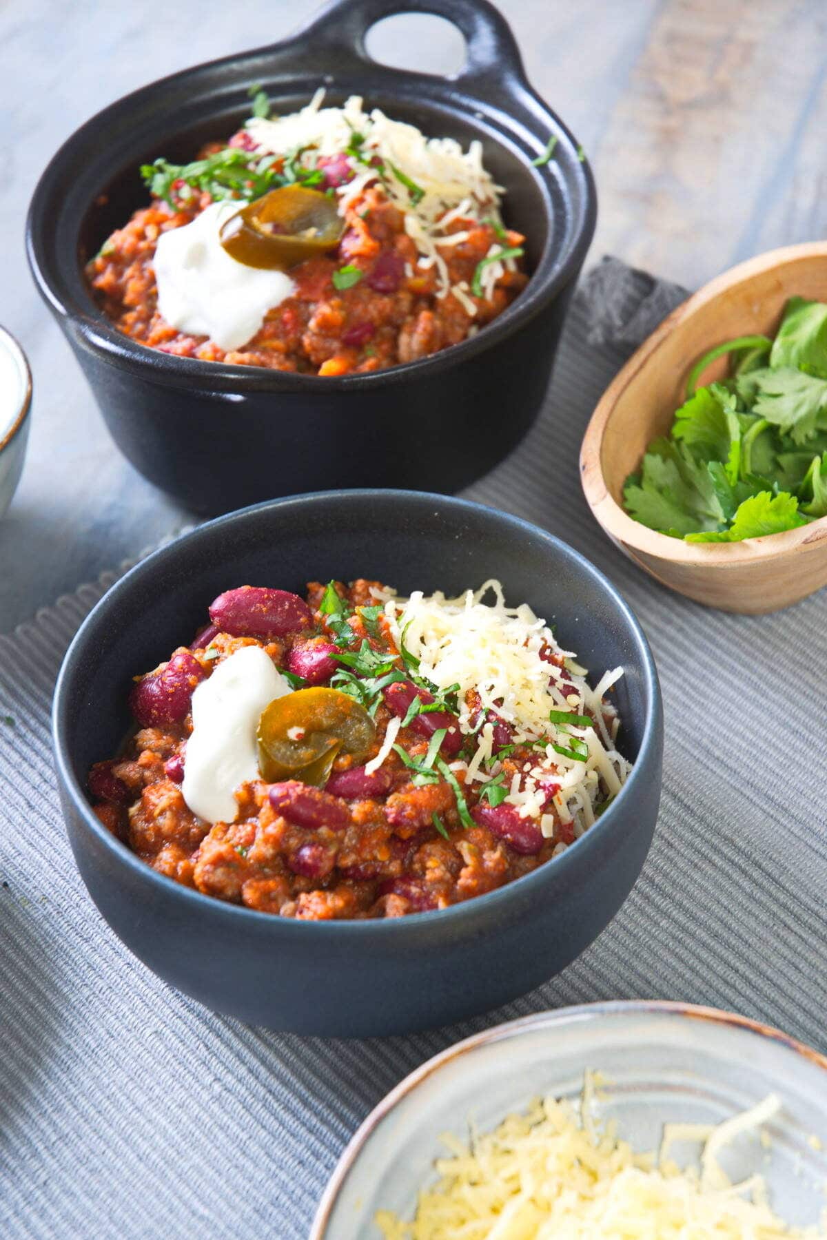 Bison chili with cheese and cilantro in black bowls.