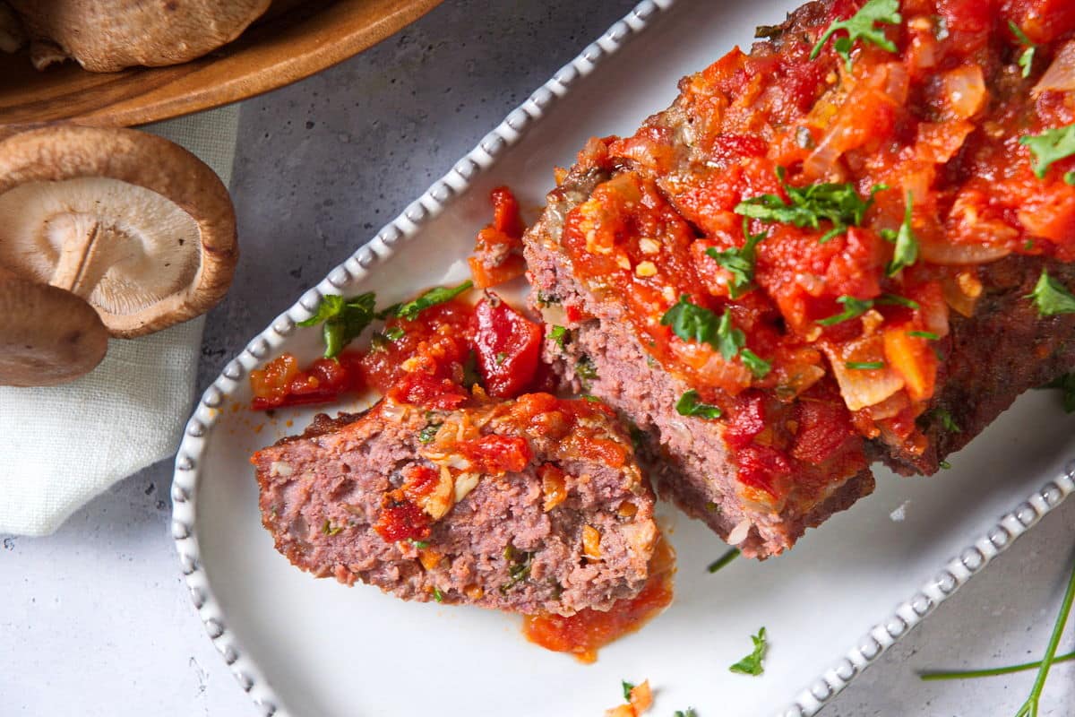 Bison meatloaf sliced on white serving dish, mushrooms on the side.