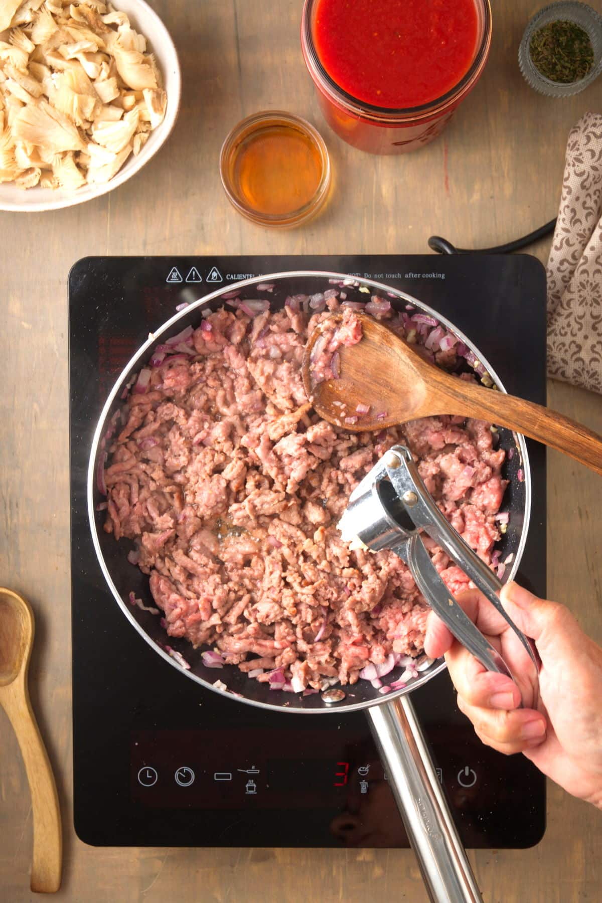 Bison ground meat in a pan and a garlic press in hand.