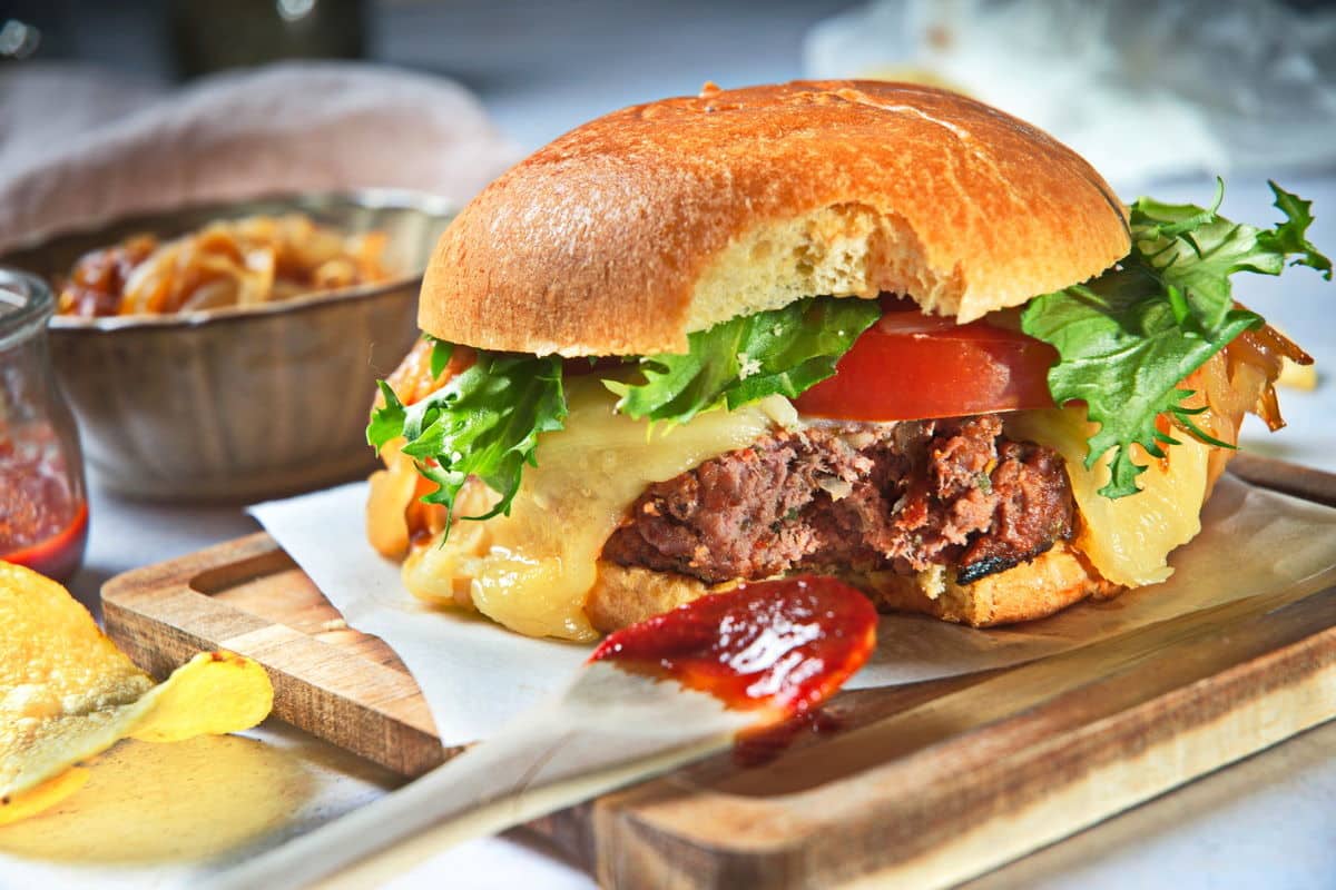 Bison burger with bite taken out of it on wooden cutting board.