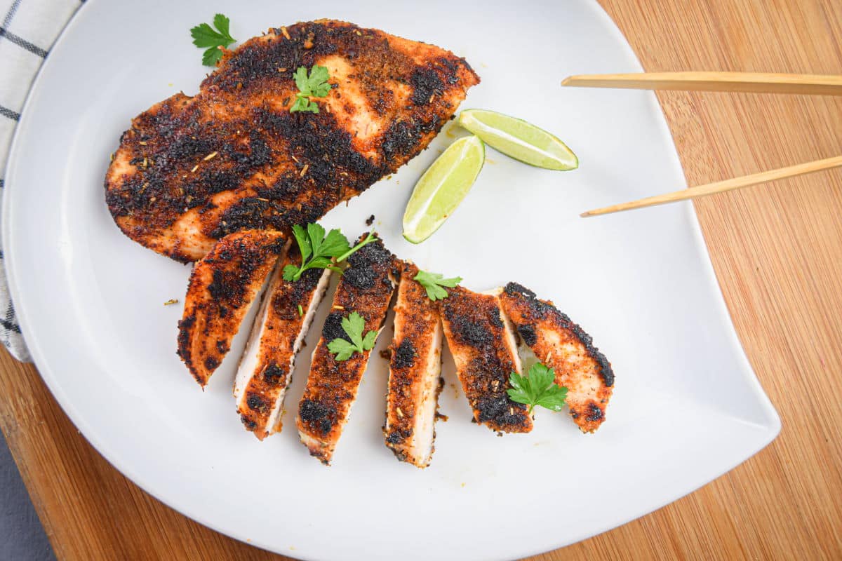 Blackened chicken breast on white plate with lime wedges.