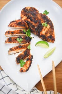 Blackened chicken breast on white plate with lime wedges.