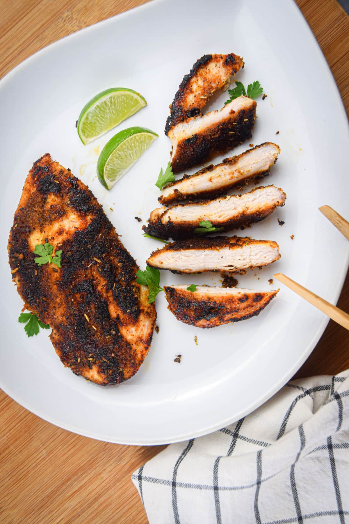 Blackened chicken breasts on white plate with lime wedges.