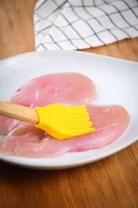 Raw chicken breast on plate with silicone brush.