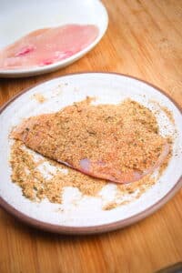 Raw chicken breast covered in blackening spices on plate.